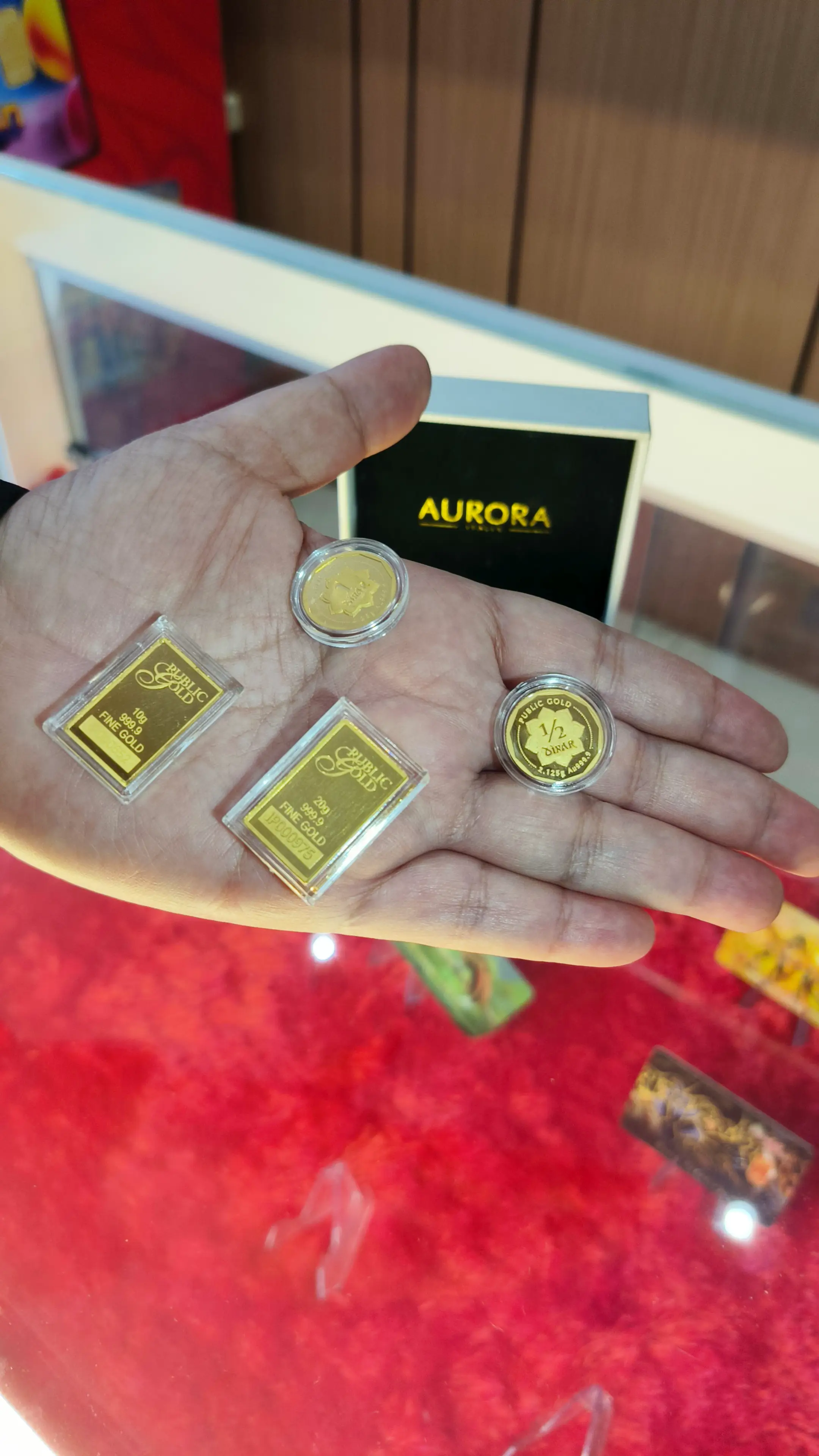 Beragam produk emas Public Gold seperti gold bar dan dinar yang ditampilkan di atas telapak tangan.