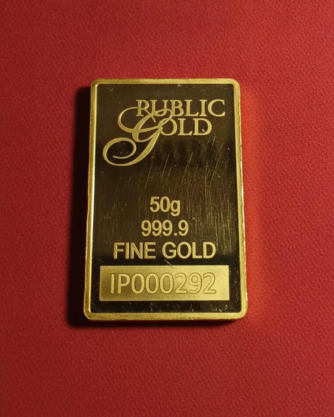 Tampilan depan batangan emas Public Gold 50g 999.9 pada latar belakang merah