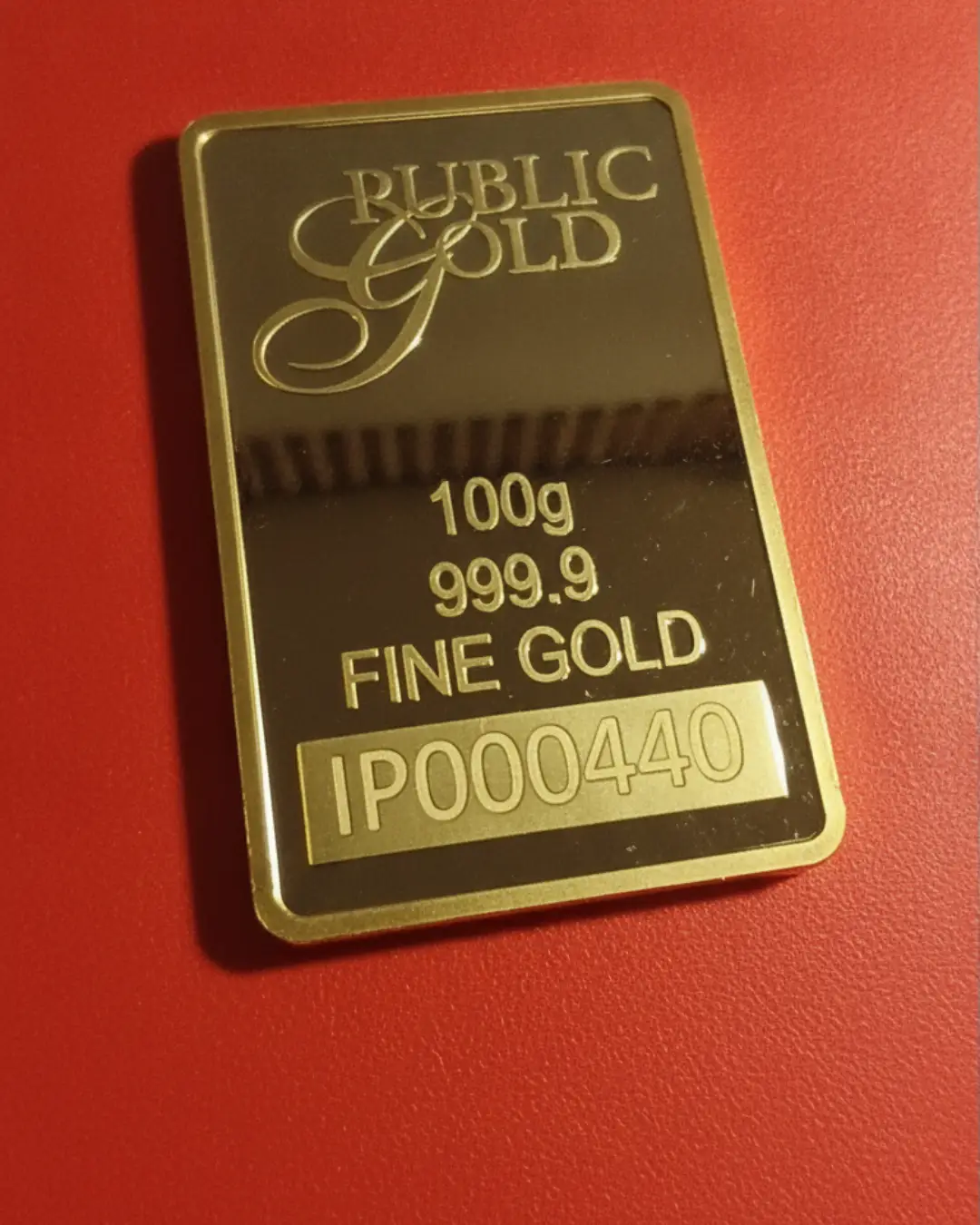Tampilan sudut batangan emas Public Gold 100g 999.9 pada latar belakang merah